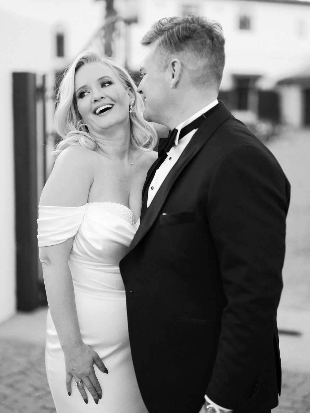 Black-and-white portrait of a wedding couple smiling at each other outdoors