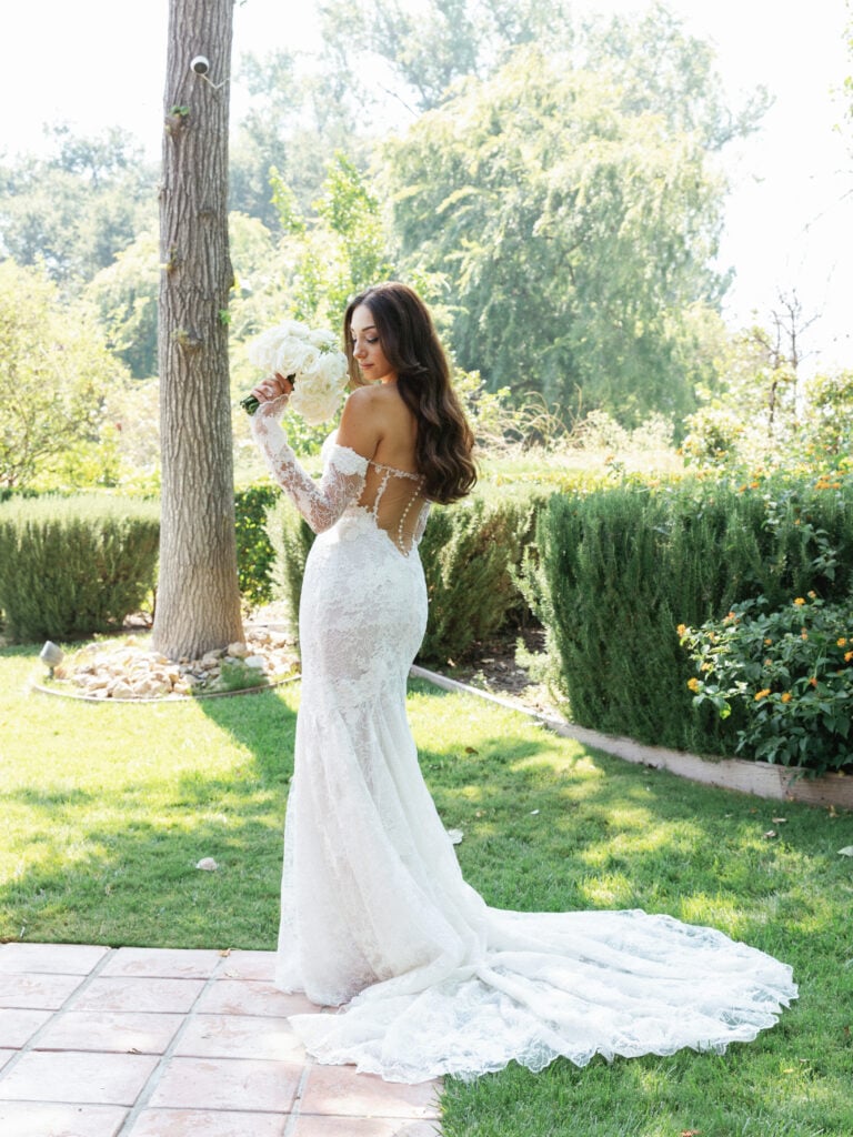 Editorial back details of a lace mermaid wedding dress and long train in an outdoor garden setting.