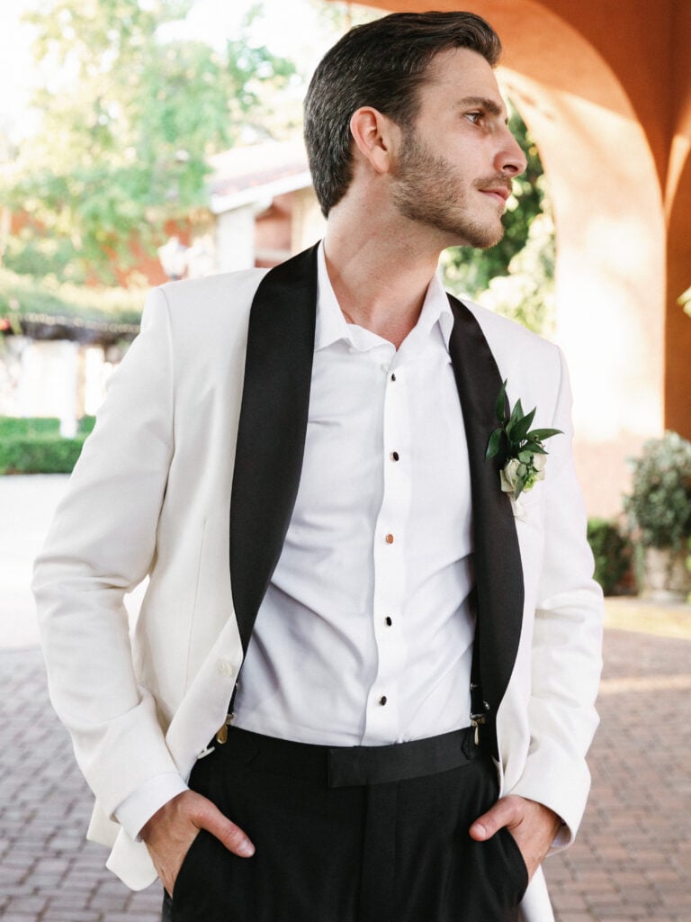Sophisticated groom style featuring a white tuxedo jacket with black satin lapels for a high-fashion black-tie look.