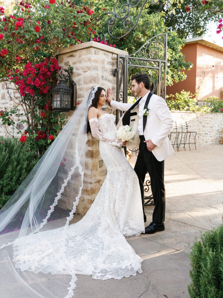 Editorial couple portrait showcasing a dramatic scalloped lace train against a rustic stone pillar.