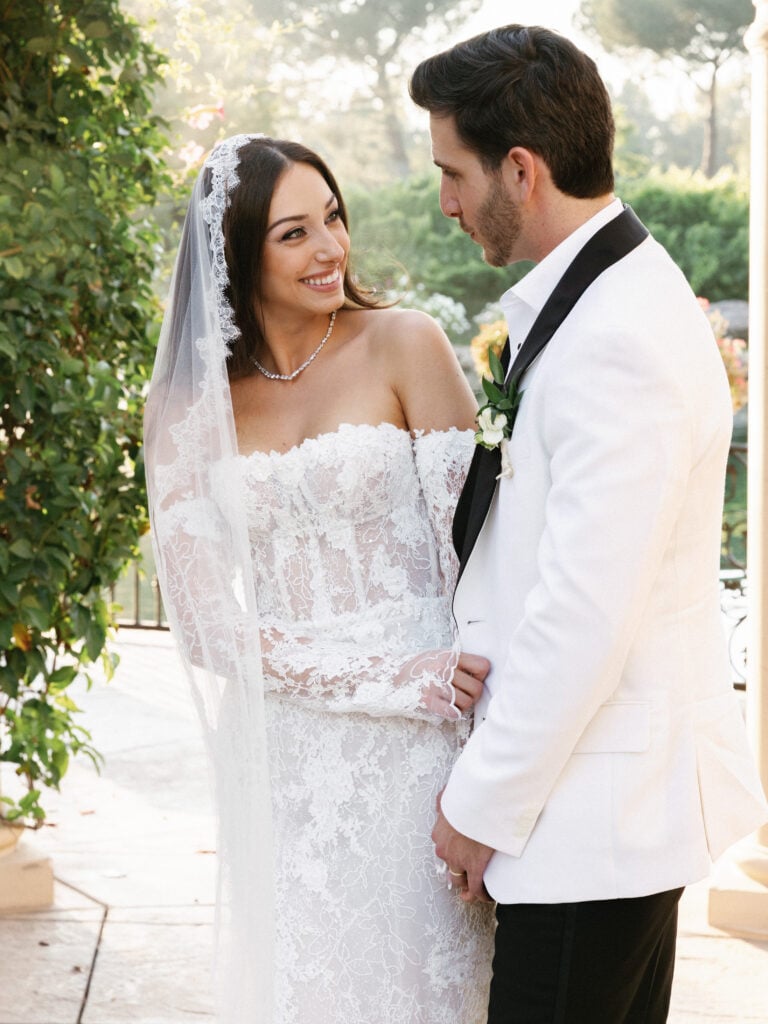 Romantic golden hour wedding portrait of a bride in a strapless lace gown and a groom in a white dinner jacket.