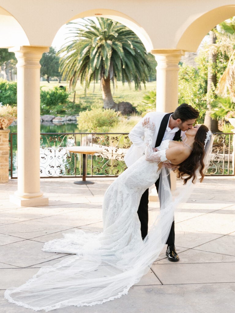 Dramatic wedding dip kiss on a luxurious estate terrace with tropical palm trees and architecture.