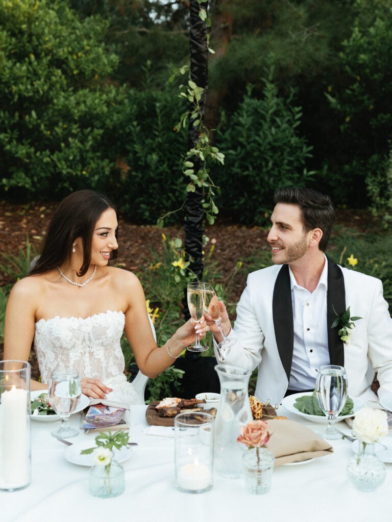 Bride and groom sharing a champagne toast at their elegant outdoor wedding reception table.