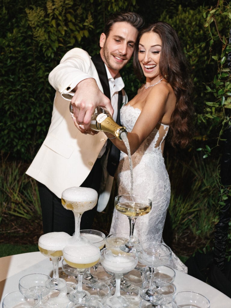 Lively champagne tower pour by newlyweds at an outdoor evening reception at Hummingbird Nest Ranch.