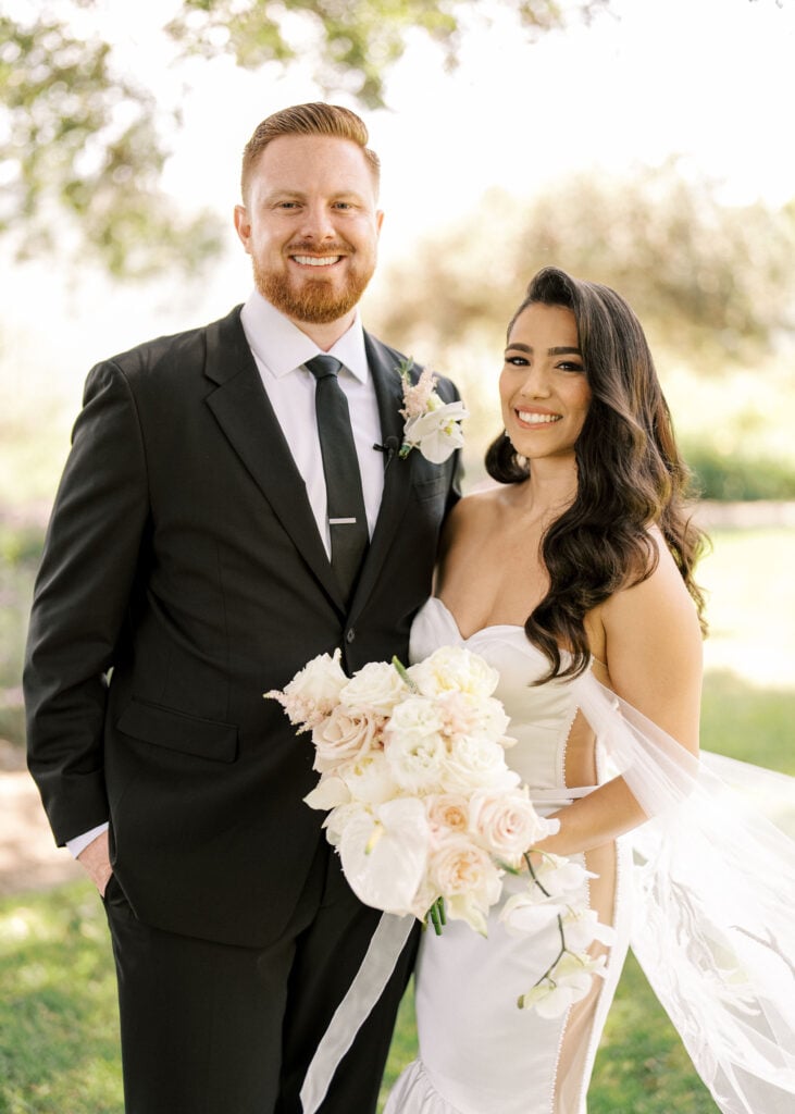 Radiant outdoor couple portrait showcasing a modern strapless gown and lush white orchid bridal bouquet in soft open shade.