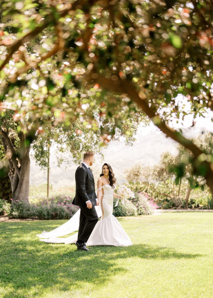 Romantic bride and groom stroll captured in dappled shade, illustrating how lush natural greenery enhances high-end wedding venue photography.