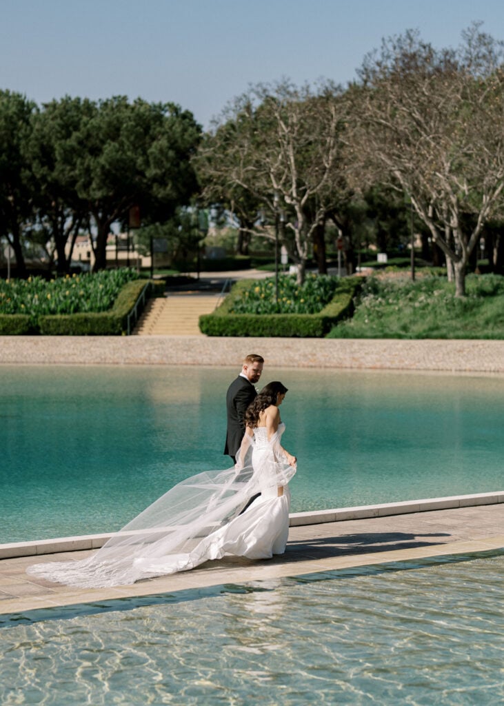 Cinematic bride and groom stroll by a turquoise reflection pool, demonstrating light-filled spaces for editorial wedding venue photography.