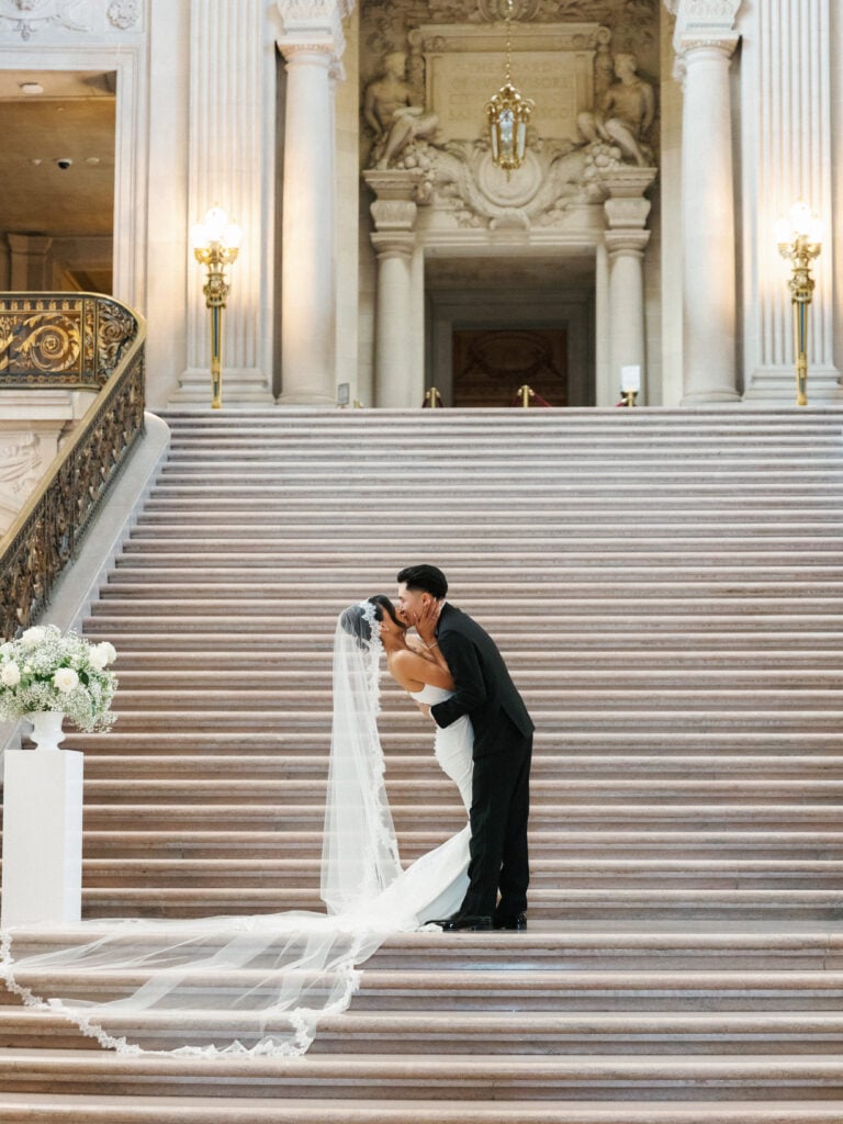 Breathtaking wedding dip kiss on the grand marble staircase at San Francisco City Hall, utilizing soft architectural light for iconic wedding venue photography.