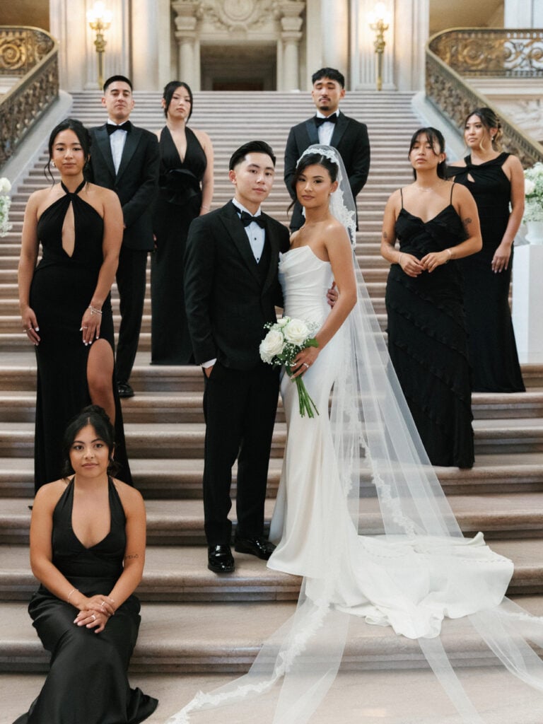 Editorial bridal party styling on a grand marble staircase, showcasing indoor light aesthetics for classic wedding venue photography.