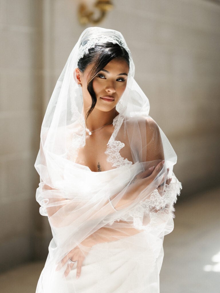 High-fashion bridal portrait utilizing soft window light to emphasize a lace mantilla veil at San Francisco City Hall.