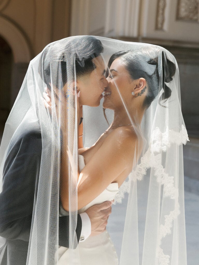 Romantic under-the-veil kiss at San Francisco City Hall, showing how historic architecture creates flattering light for wedding portraits.