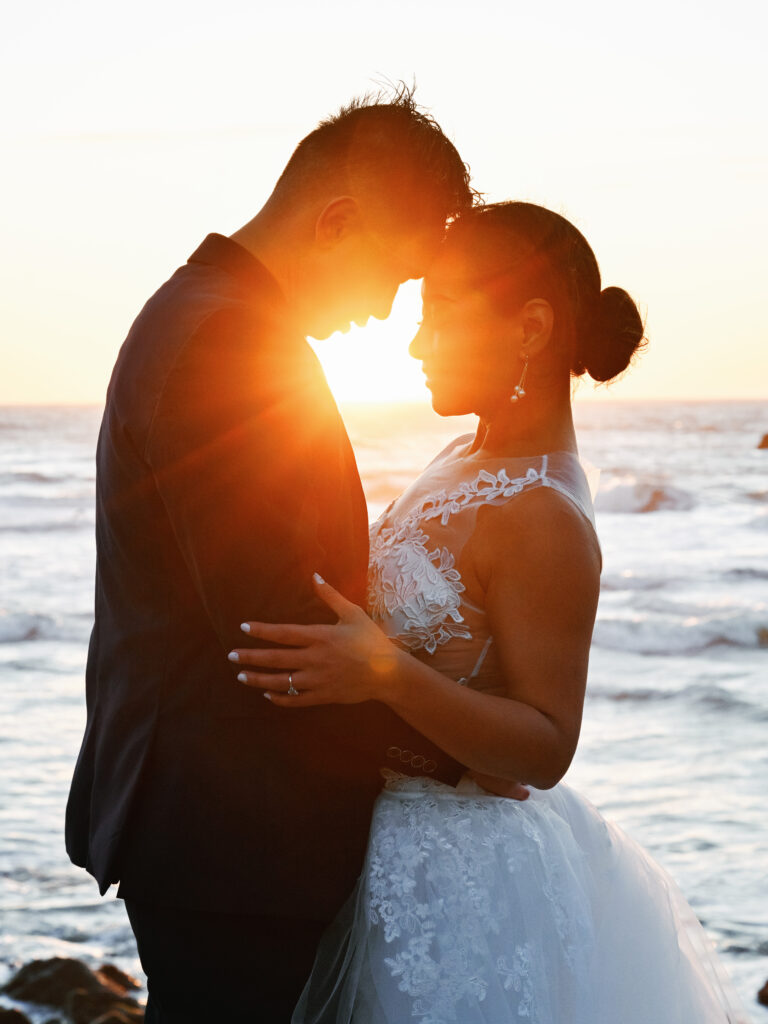Romantic golden hour couple portrait with dramatic sun flare effects against the Malibu coastal sunset.