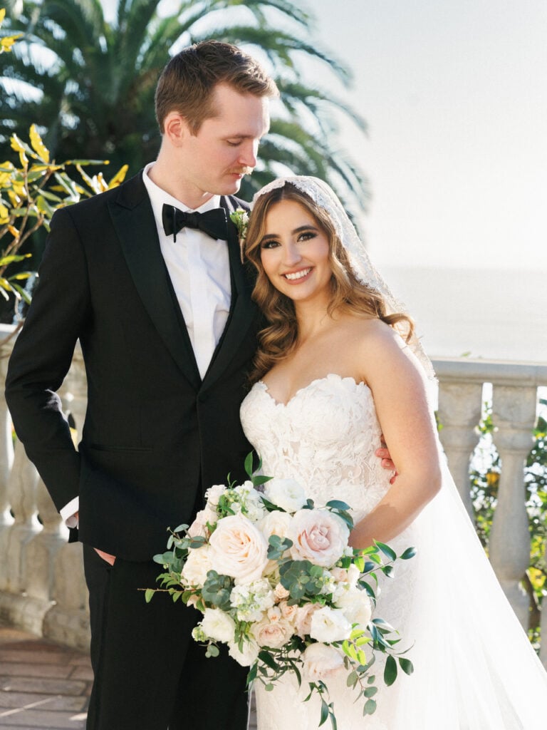 Radiant newlywed portrait by a coastal stone balustrade, using soft natural backlighting secrets for high-end wedding venue photography.