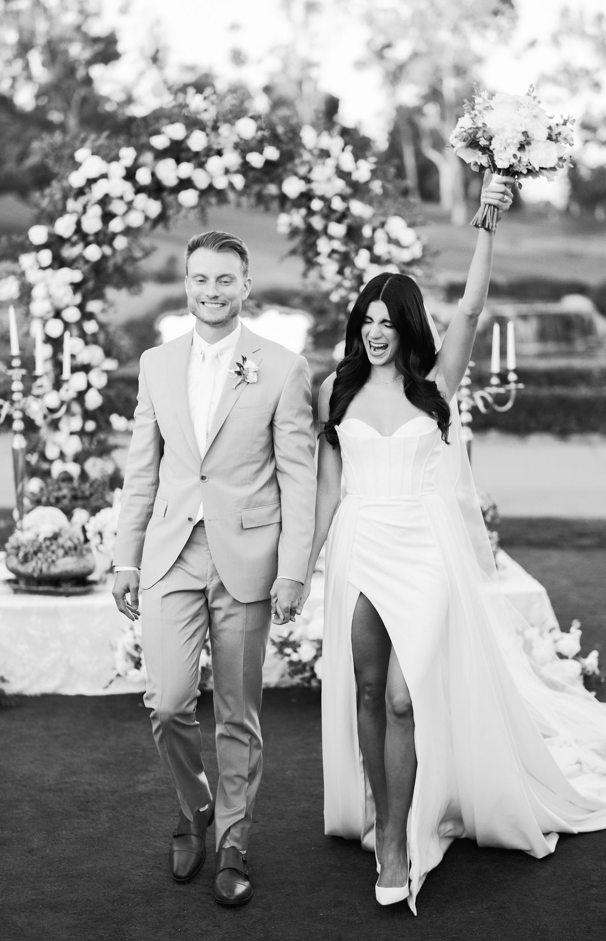 Newlyweds walking hand in hand beneath a floral wedding arch