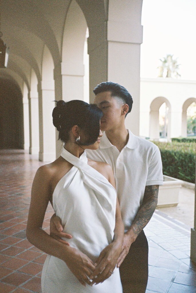 Intimate film wedding photography of a couple embracing under a historic stucco archway, capturing the bride's chic silk halter gown.
