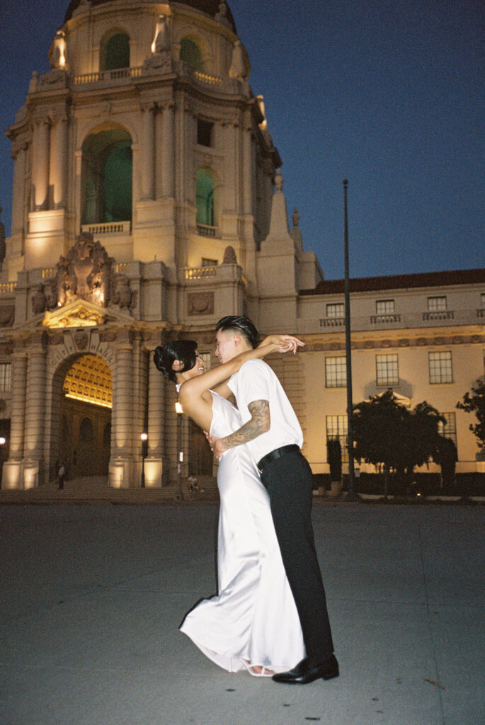 Candid night film wedding photography of a stylish couple dancing in front of an illuminated historic city hall.