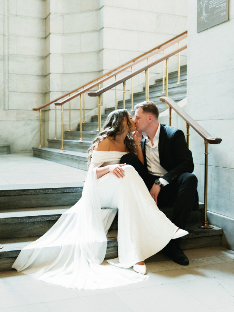 Elegant wedding photo ideas featuring a luxury couple kissing on a historic marble staircase inside the New York Public Library.