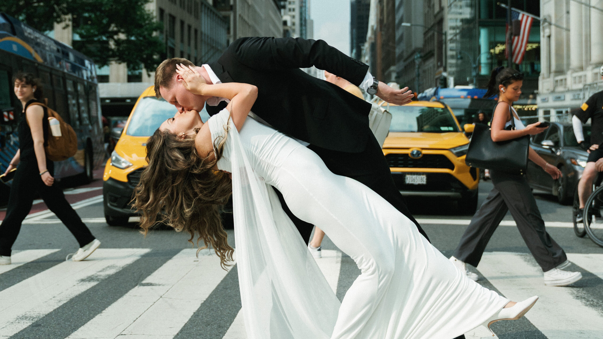 Couple kiss during a dip on a city street beside yellow taxis.