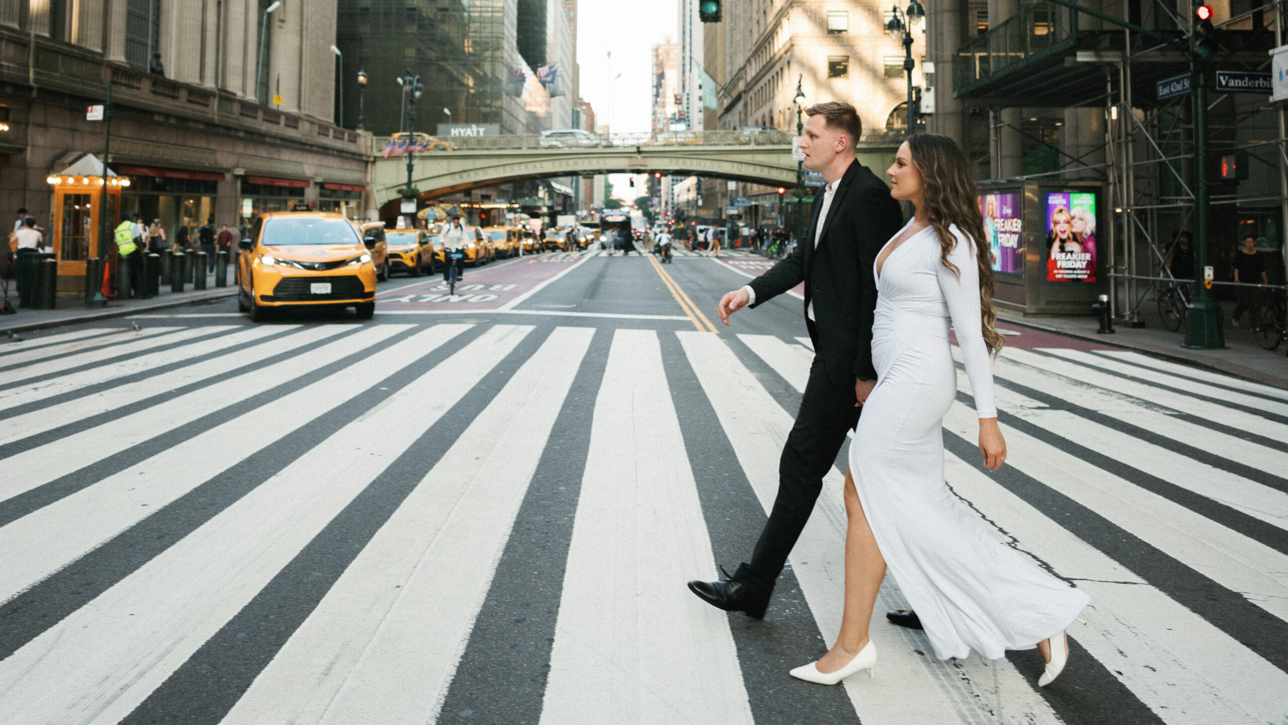 Iconic Manhattan wedding photo ideas featuring a luxury couple walking across a 42nd Street crosswalk near Grand Central Terminal.