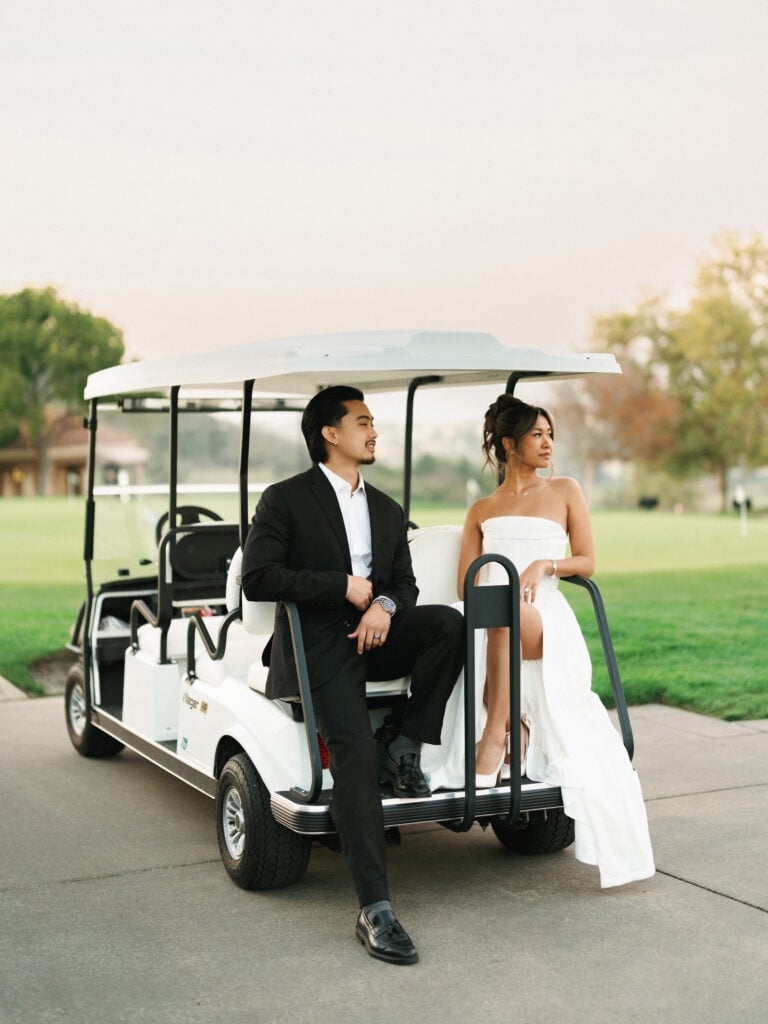 Chic bride and groom posing naturally on a white golf cart at a scenic luxury resort club, capturing authentic moments for modern editorial wedding photography.