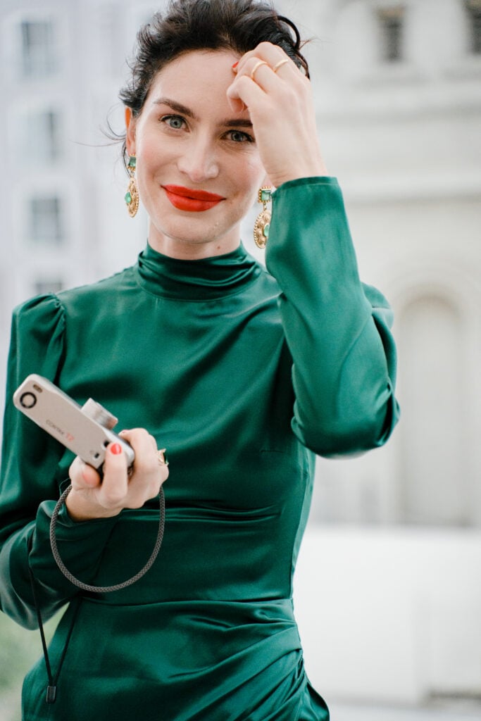 Chic female guest in a high-neck emerald green silk dress holding a vintage Contax T2 film camera, inspiring editorial wedding weekend coverage moments.