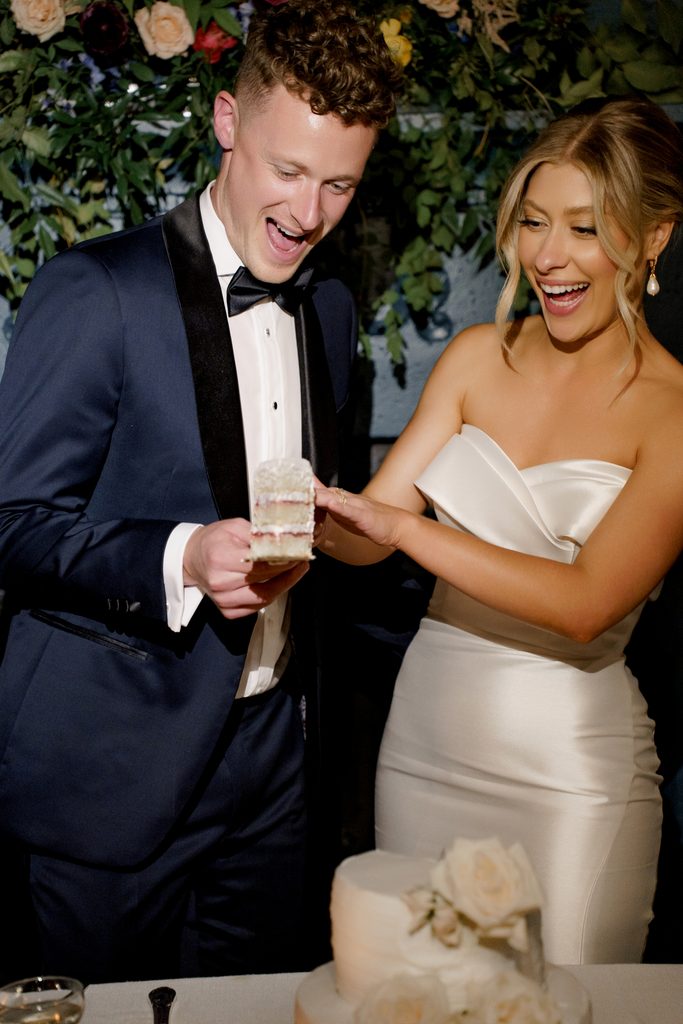 Joyful wedding photo ideas capturing a candid moment of a bride and groom laughing while cutting their luxury cake.