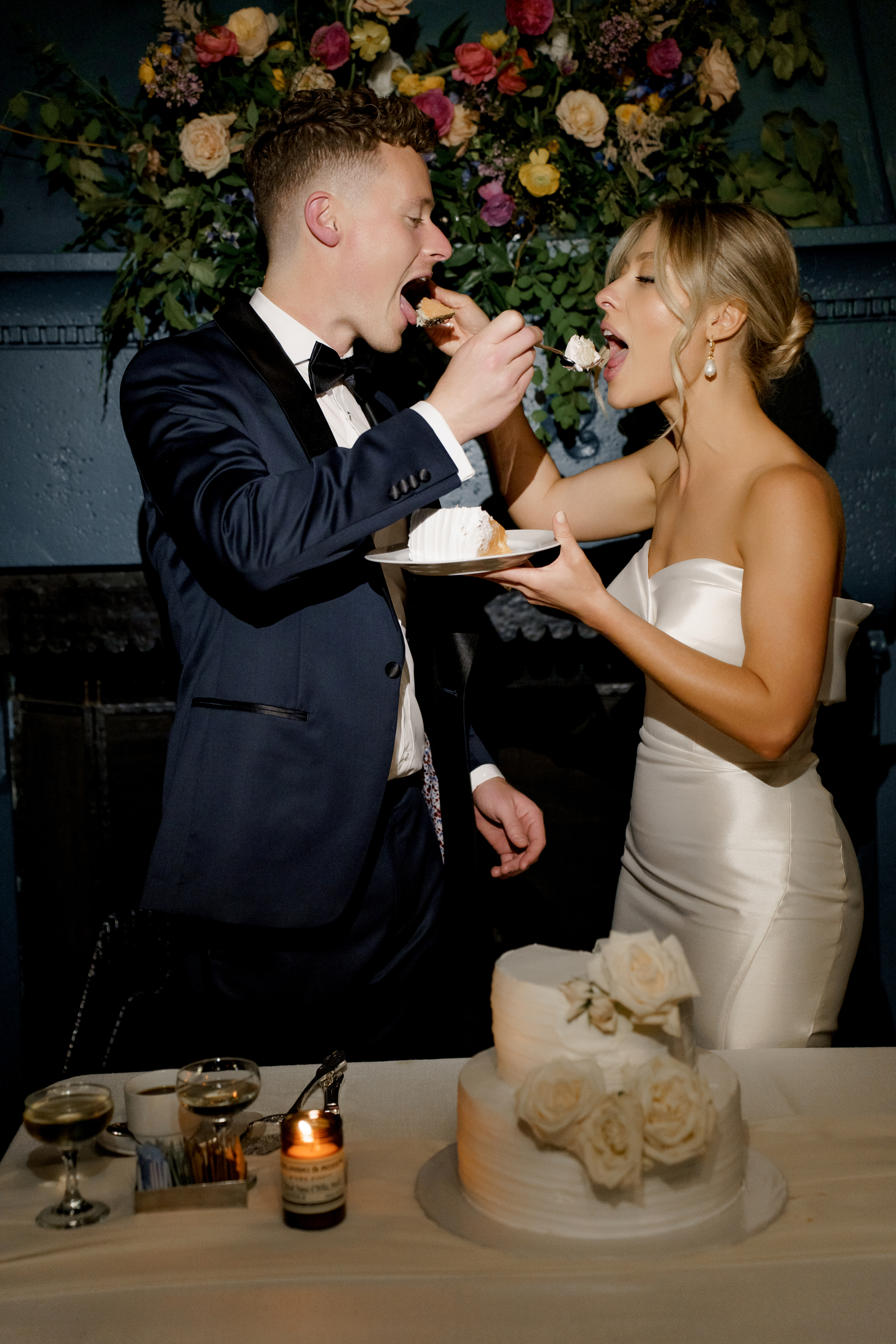 Bride and groom feeding each other wedding cake across a decorated reception table.
