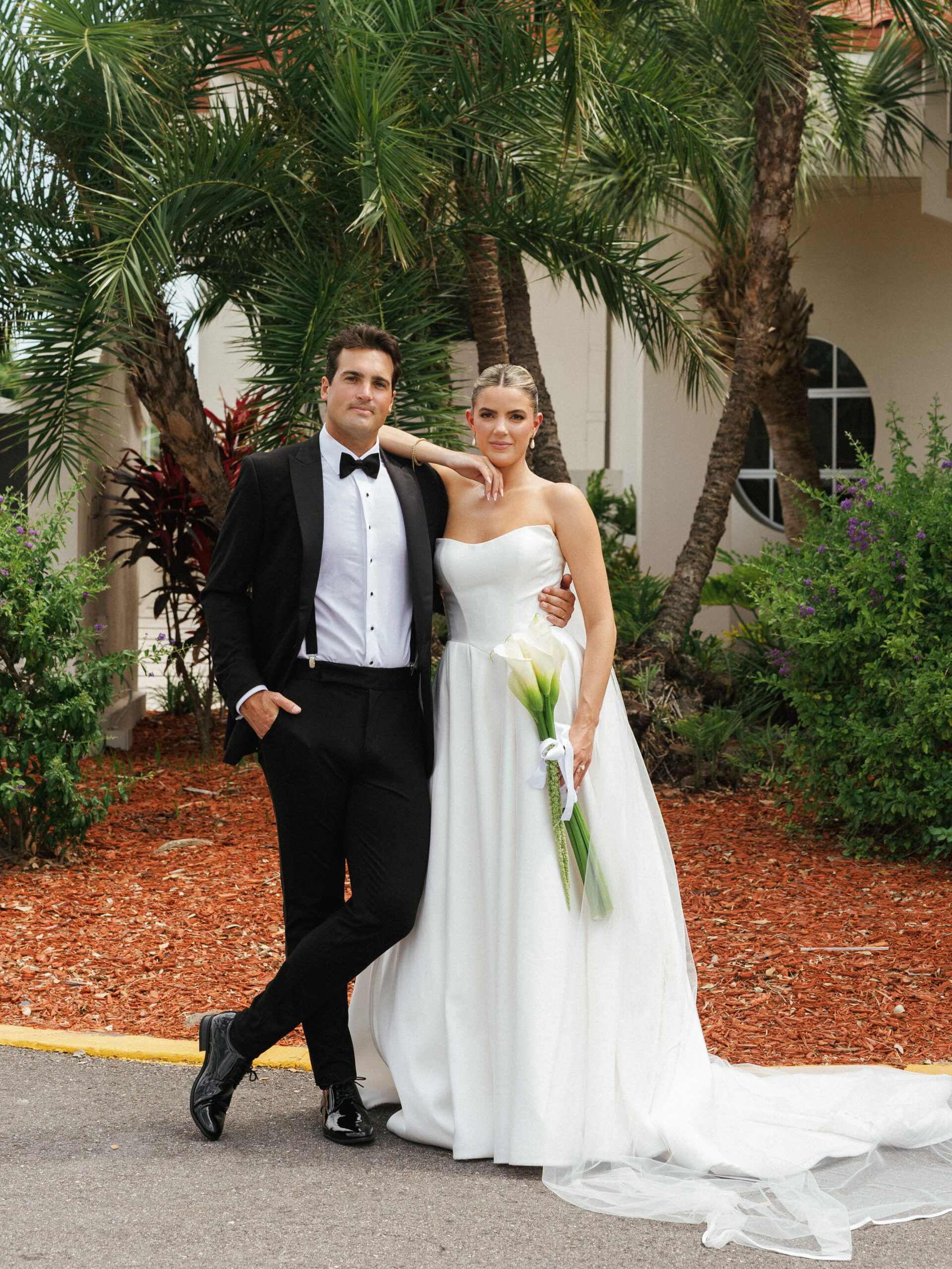 Tropical luxury wedding photo ideas featuring a sophisticated couple posing on a resort lawn surrounded by lush palm trees.