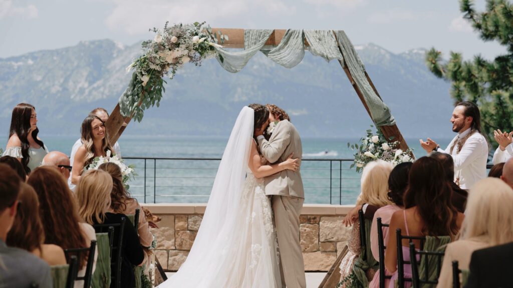 Bride and groom kissing under a wooden wedding arch with mountain and lake views