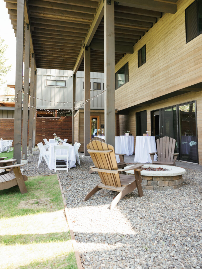 Wooden adirondack chairs arranged around a stone fire pit on a gravel patio at a mountain lodge reception