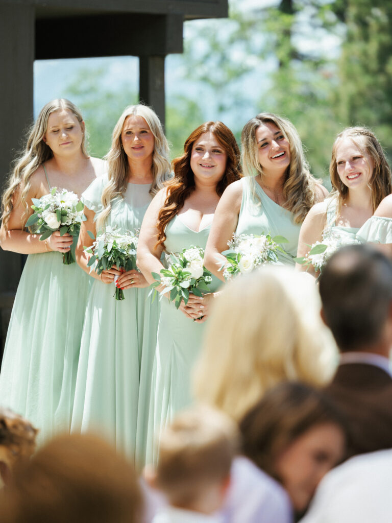 Bridesmaids in matching sage green dresses holding bouquets and watching the ceremony from the altar