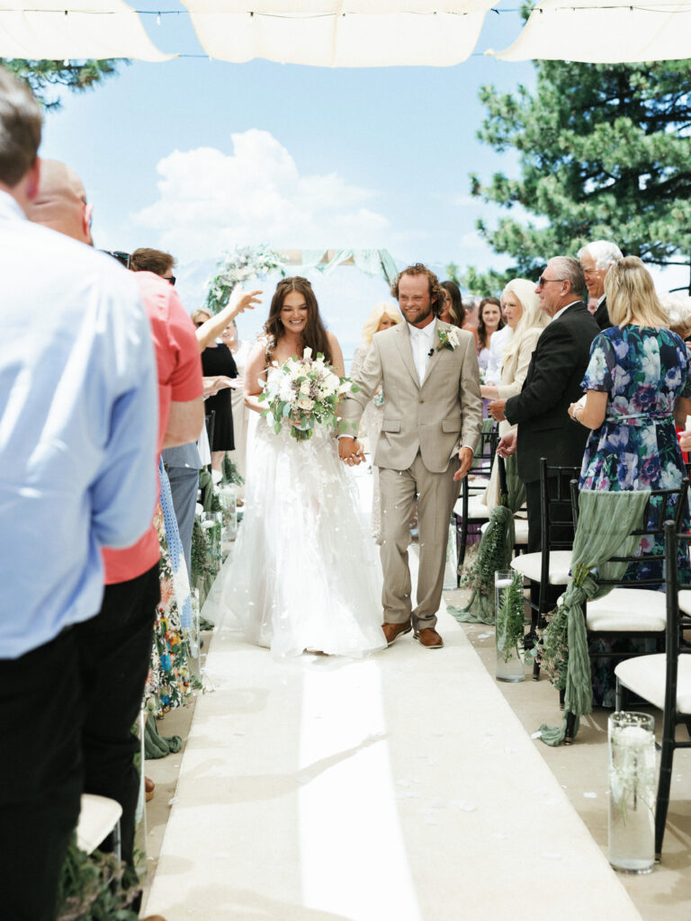 Smiling bride with a lush bouquet and groom in a tan suit walking past cheering guests fine art Lake Tahoe wedding photography