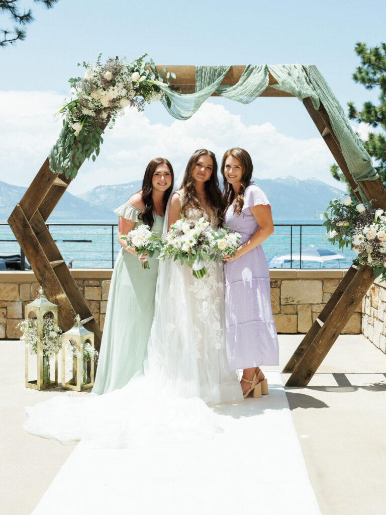 Bride with bridesmaids in pastel sage and lavender dresses on a sun drenched lakeside terrace Lake Tahoe wedding photographer