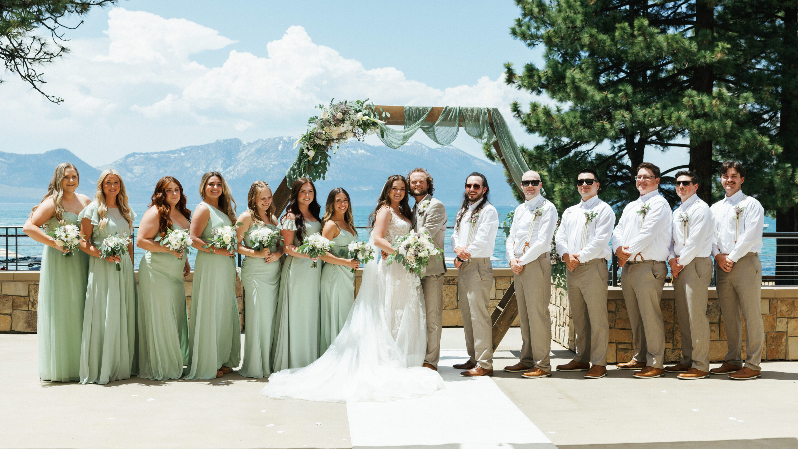 Bride and groom with wedding party in sage green gowns and tan trousers at a lakeside terrace, by a Lake Tahoe wedding photographer.