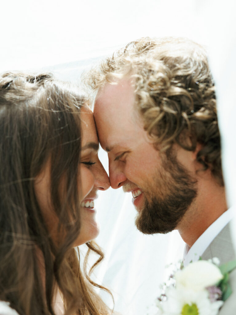 Close up portrait of a smiling bride and groom sharing an intimate moment under a veil by a Lake Tahoe wedding photographer