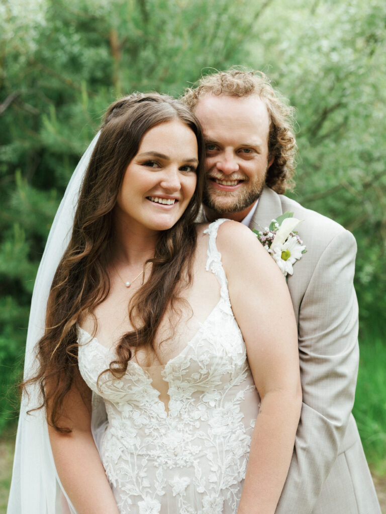 Groom embracing his smiling bride from behind in a lush green forest fine art Lake Tahoe wedding photography
