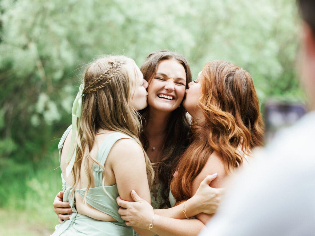Bridesmaids kissing a smiling bride on the cheeks during an outdoor wedding portrait session
