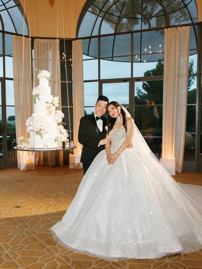 Glamorous newlyweds posing by a suspended wedding cake at The Resort at Pelican Hill, showcasing a luxury indoor alternative for a wedding rain plan.