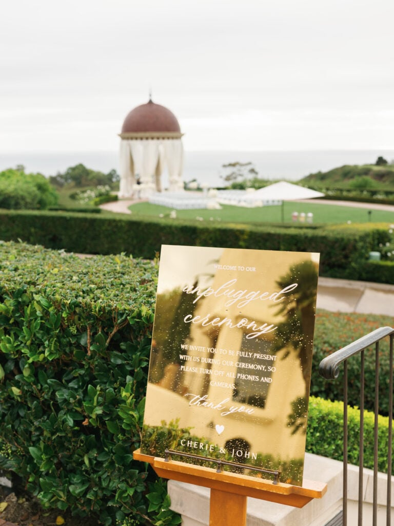 Custom gold acrylic unplugged ceremony sign at The Resort at Pelican Hill, captured under flattering overcast wedding day light.