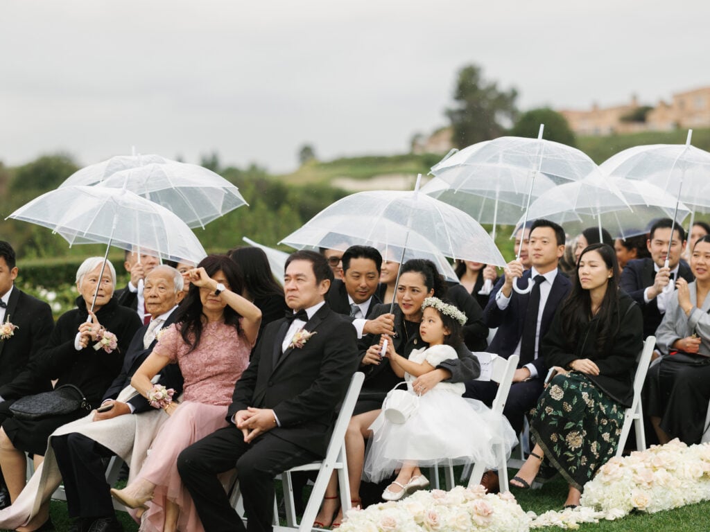 Sophisticated wedding guests with clear umbrellas at an outdoor ceremony, demonstrating a thoughtful wedding rain plan for guest comfort.