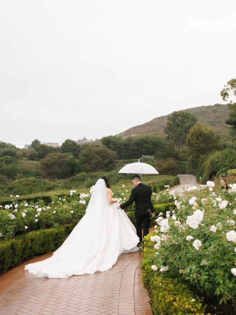 Romantic newlyweds walk through a lush white rose garden, showing a seamless rain alternative that keeps the luxury story alive.