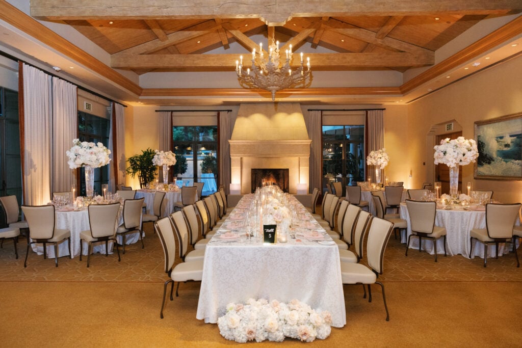 Lavish indoor wedding reception ballroom featuring tall floral centerpieces and a grand fireplace, showcasing an upscale wedding rain plan alternative.