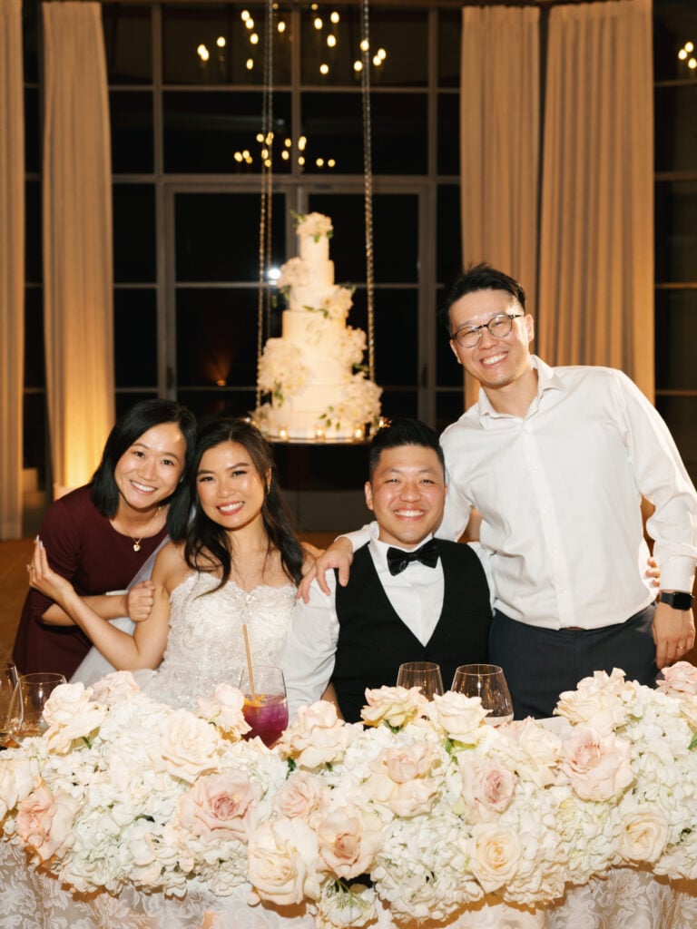 Lively newlywed and guest moments at a floral-filled sweetheart table, illustrating a seamless indoor reception wedding rain plan.