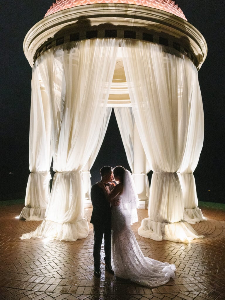 Cinematic night wedding portraits under the illuminated Pelican Hill rotunda, showing a creative execution of a luxury wedding rain plan.