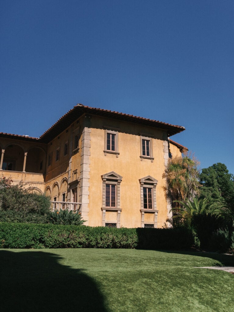 Luxury historic Italian-style villa with a manicured green lawn under a clear blue sky, selected for an exclusive destination wedding travel experience in California.