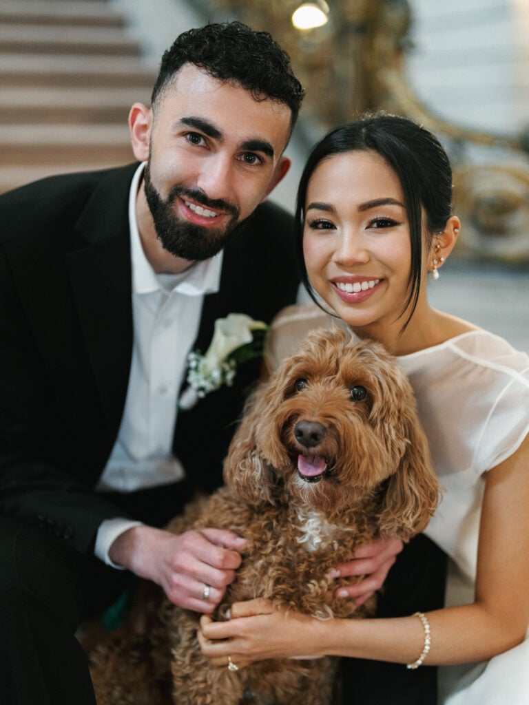 Smiling bride and groom posing naturally with their fluffy brown dog during an emotional editorial wedding photography session inside San Francisco City Hall.