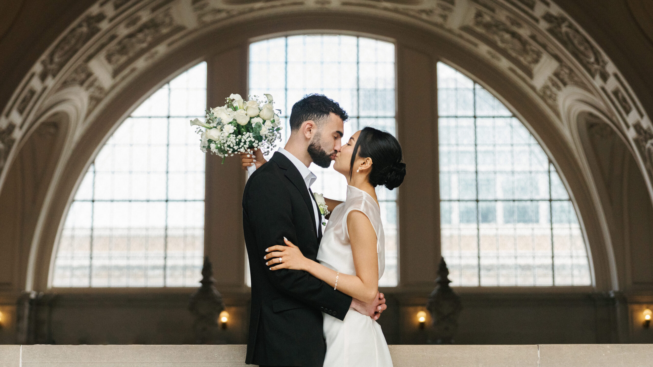 Romantic San Francisco City Hall wedding photo ideas featuring an elegant couple kissing in front of a grand arched window.