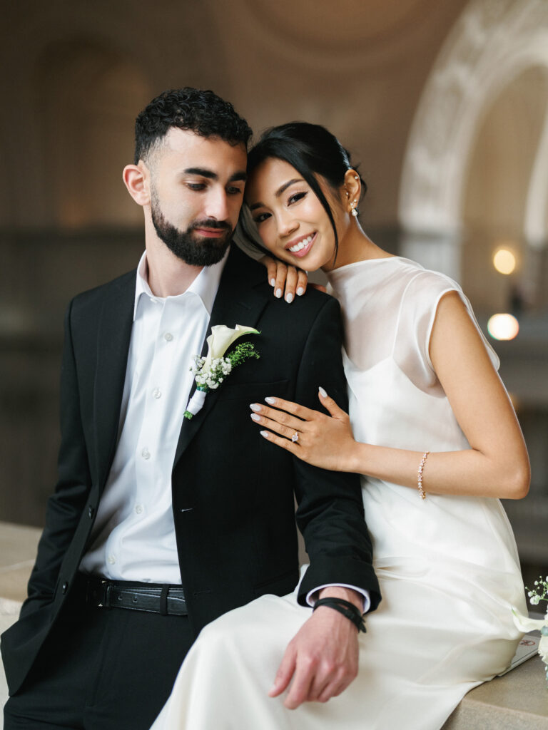Close-up fine-art wedding photo ideas capturing a joyful bride leaning on her groom, highlighting her diamond engagement ring and bracelet.