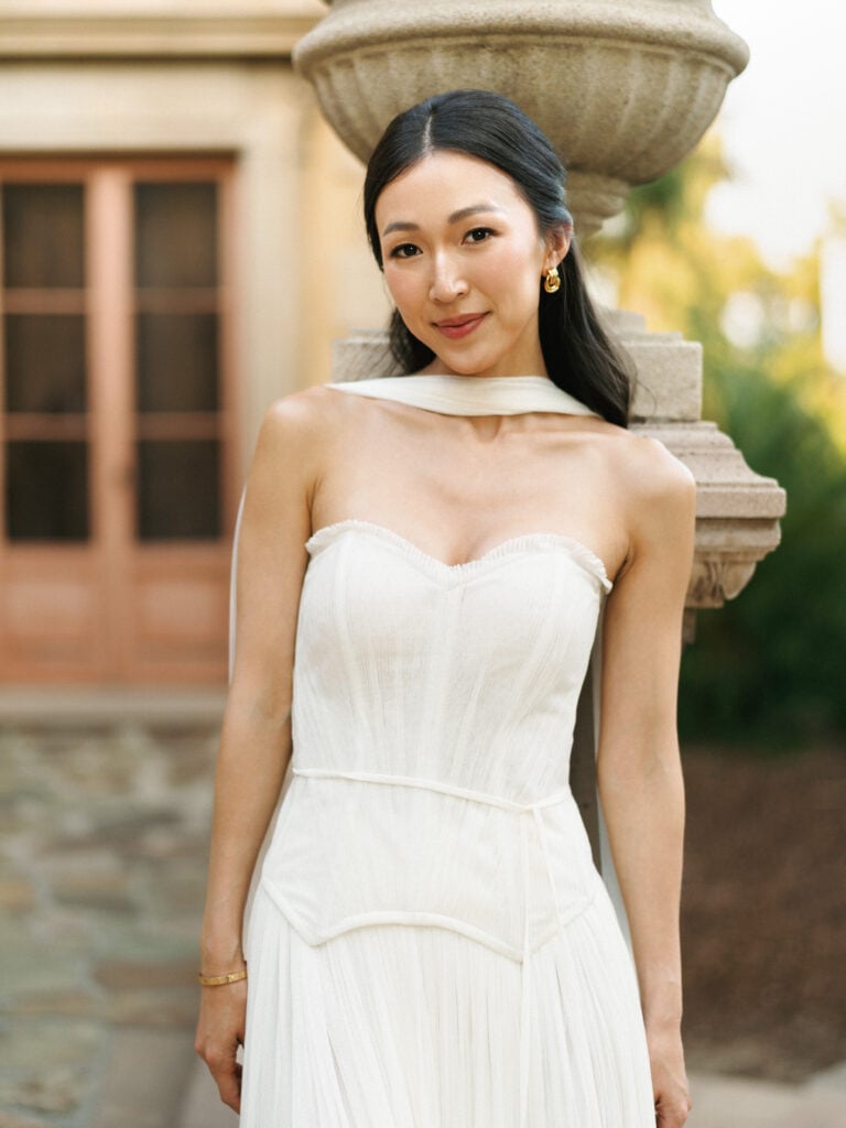 Sophisticated bride showcasing a strapless corset bodice wedding dress with a chiffon scarf at a California estate, inspiring editorial destination wedding travel style.
