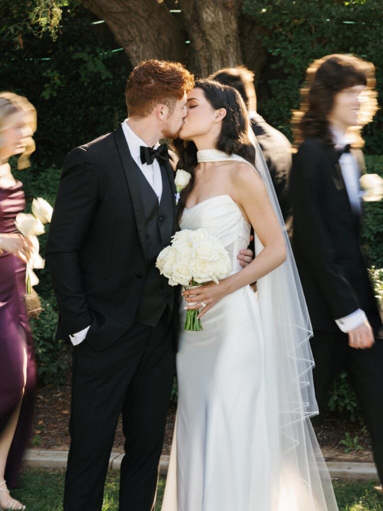 Romantic bride and groom sharing a passionate kiss while guests blur in motion around them, capturing an authentic artistic moment for editorial wedding photography.